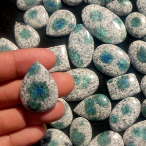 May include: A collection of polished, teardrop-shaped gemstones with a white and blue speckled pattern. The stones have a variety of sizes and shapes.