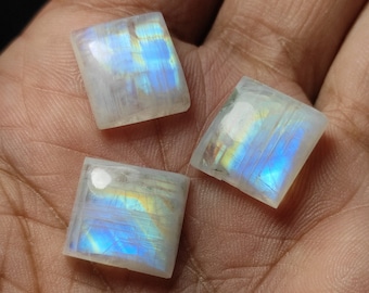 May include: Three iridescent moonstone cabochons, each cut into a square shape. The stones are a milky white color with a blue and yellow sheen.