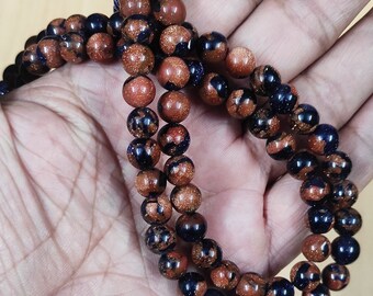 May include: A strand of brown and blue gemstone beads. The beads are round and have a speckled appearance. The beads are strung on a clear string.