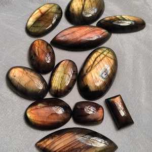 May include: A collection of 11 labradorite gemstone cabochons in various shapes and sizes. The stones are a mix of dark green, black, and gold colors with iridescent flashes.