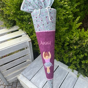 Könnte beinhalten: Ein rosa-grüner Schultüte mit einem weißen Kordelzug und einem Ballerina-Motiv. Die Tüte ist mit dem Namen "Anny" personalisiert.