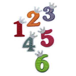 Könnte beinhalten: Sechs bunte Filz-Zahlen mit silbernen Kronen oben drauf. Die Zahlen sind 1, 2, 3, 4, 5 und 6.