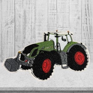 Könnte beinhalten: Gestickter Aufnäher eines grünen und schwarzen Traktors mit roten Rädern und Frontlader. Der Traktor hat eine weiße Kabine. Der Aufnäher ist vor einem hellen Holzmaserungshintergrund platziert. Für Kleidung oder Accessoires.
