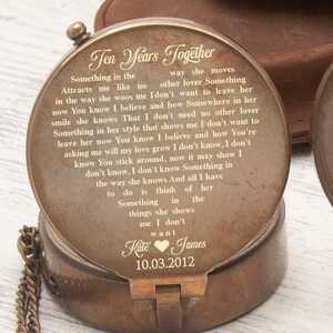 May include: A brass compass with a chain and a lid that opens to reveal a personalized message. The message reads "Ten Years Together" and includes a poem about love. The lid also has the date "10.03.2012" engraved on it. The compass is on a wooden surface.