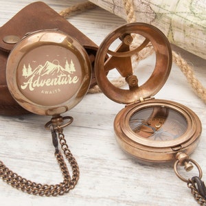 May include: A brass compass with a chain and a leather pouch. The compass face has a compass rose and the words "Adventure Awaits" are engraved on the lid.