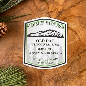 May include: White sticker with black text and a green outline. The sticker says "Summit Success" and features a black and white illustration of a mountain range. The text below the mountain says "Old Rag, Virginia, USA, 3,284 ft, 38.5517° N, -78.3158° W, Fortune Favors The Bold."