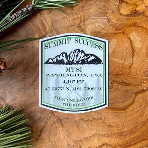 May include: White sticker with a green mountain range illustration and the text "Summit Success", "MT SI", "Washington, USA", "4,167 FT", "47.5077° N, 121.7398° W", "Fortune Favors The Bold".