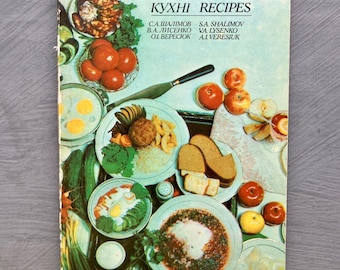 May include: A vintage cookbook titled "Ukrainian Cookery Recipes" with a cover featuring a colorful arrangement of prepared dishes. The cover text is in both English and Ukrainian. The image showcases various plates of food, including eggs, tomatoes, and bread.