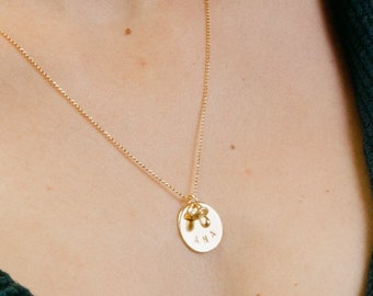 May include: A gold chain necklace with a round pendant that says "ANA" and a small gold charm attached to the top of the pendant.