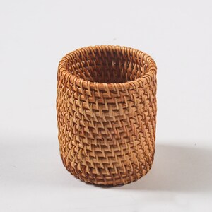 May include: A woven wicker basket in a natural brown colour. The basket is cylindrical in shape and has a woven pattern.