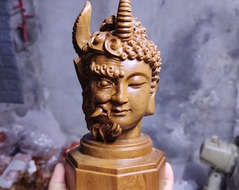 May include: A wooden sculpture of a Buddha with a demon face on one side. The sculpture is carved in detail and has a dark brown colour.