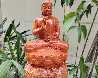 May include: A hand-carved wooden statue of Buddha sitting in meditation on a lotus base. The statue is made of reddish-brown wood and has a serene expression.