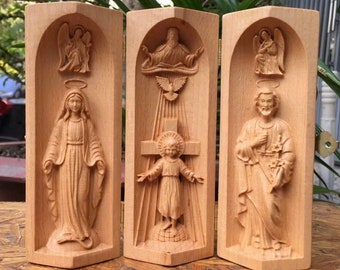 May include: A wooden triptych with three panels, each featuring a carved religious figure. The center panel depicts Jesus Christ on the cross, while the left panel shows the Virgin Mary and the right panel shows Saint Joseph. The panels are hinged and can be folded closed.
