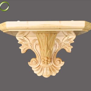 以下が含まれることがあります： 装飾的な彫刻が施された明るい色の木製ウォールシェルフ。シェルフは長方形の上面と、花柄とスクロールデザインが特徴の装飾ブラケットを備えています。木材は自然な仕上がりで、素材の木目と質感を際立たせています。