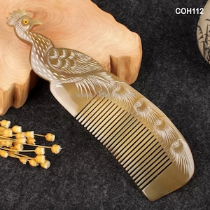 May include: A brown and white comb with a peacock design. The comb is made of horn and has a fine-toothed design.