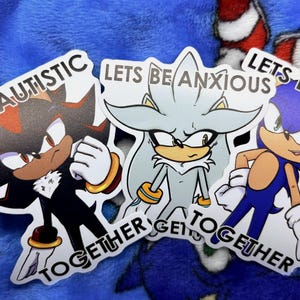 May include: Three cartoon character stickers with the phrases "Lets Be Autistic", "Lets Be Anxious", and "Lets Be ADHD". The stickers feature characters in black, silver, and blue with the words "Together" at the bottom.