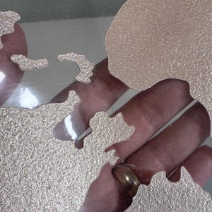 May include: A set of metallic gold-colored stencils in the shape of continents. The stencils are on a clear surface.