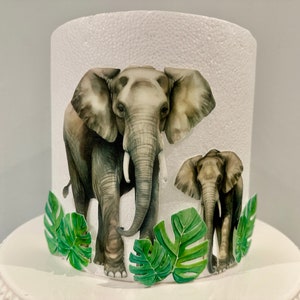 May include: A white cylinder with a textured surface, decorated with two watercolor illustrations of elephants and green tropical leaves. The larger elephant is facing forward, while the smaller elephant is facing to the right.