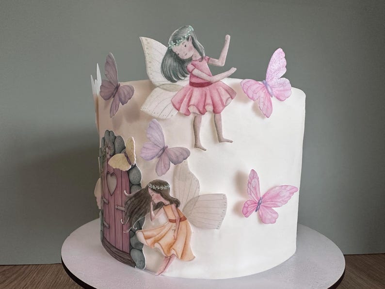 May include: A white cake decorated with fondant butterflies and fairies. The cake features a small pink door with a heart-shaped window and a stone wall.