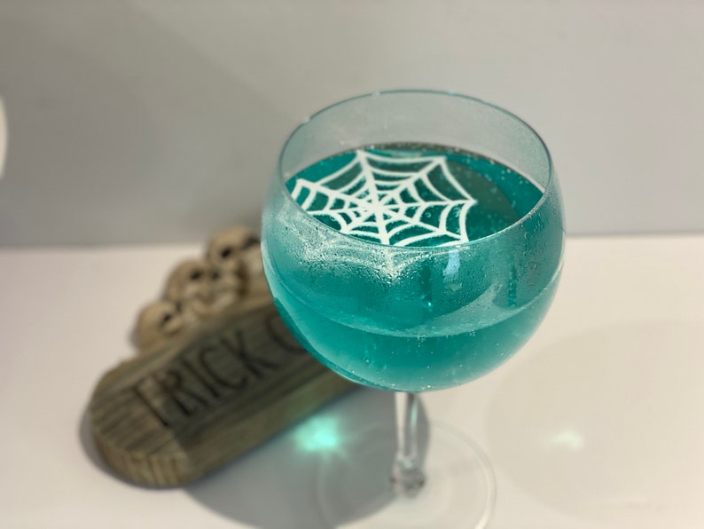May include: A glass of blue liquid with a white sugar spiderweb design on top.