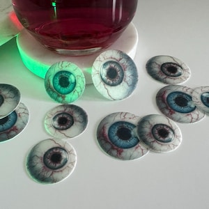 Puede incluir: Una colecci&oacute;n de 12 adornos comestibles para pasteles en forma de ojo con detalles realistas. Los adornos son blancos con venas rojas e iris azules. Algunos de los adornos tienen un iris verde.