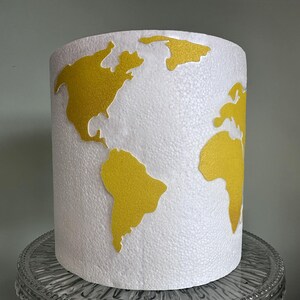 May include: White lampshade with a gold world map design. The map is raised and textured.
