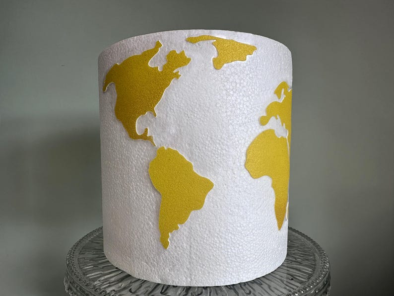 May include: White lampshade with a gold world map design. The map is raised and textured.