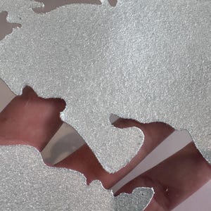 May include: A silver glitter world map stencil. The stencil is made of a thin, flexible material and has a detailed outline of the continents and oceans.