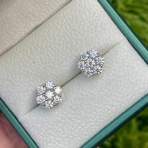 May include: A pair of flower-shaped stud earrings. Each earring has a cluster of small, round, clear gemstones set in a silver or white metal. The earrings are presented in a green jewellery box with a white interior.