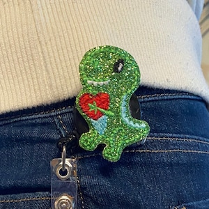 May include: A blue denim jean pocket with a clear plastic badge holder. The badge holder has a photo of a woman with pink hair and a pink and black outfit. The text on the badge reads "NON-GOVERNMENT ORGANIZATION REGISTRATION CARD", "Name Kairi Openhiemer", "ID Number 22-57-9658-652-62", "D.O.B 03-23-1992", and "Kairi CARD HOLDER'S".