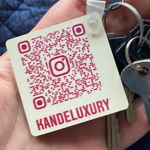 May include: A white square keychain with a pink QR code and the text "KANDELUXURY" in pink. The keychain is attached to a set of keys.