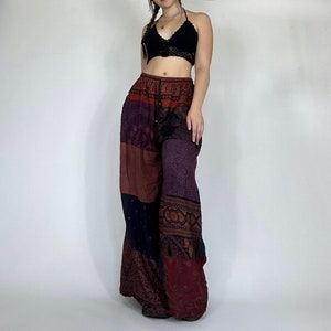 Puede incluir: Pantalones de patchwork multicolor con cintura alta y piernas anchas. Los pantalones están hechos de una tela suave y fluida y presentan una variedad de patrones florales y geométricos en tonos rojos, morados, negros y marrones.