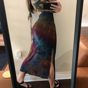 May include: A tie-dye skirt with a high slit and a matching crop top. The skirt features a mix of brown, blue, and purple hues. The crop top is green and brown. The outfit is captured in a mirror.