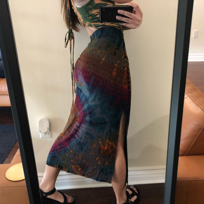 May include: A tie-dye skirt with a high slit and a matching crop top. The skirt features a mix of brown, blue, and purple hues. The crop top is green and brown. The outfit is captured in a mirror.
