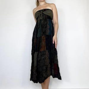 Könnte beinhalten: Ein trägerloses Patchwork-Kleid in Grün-, Braun- und Schwarztönen. Das Oberteil ist olivgrün mit einem geknoteten Detail, und der Rock hat eine Vielzahl von gemusterten Stoffquadraten. Das Kleid hat einen fließenden, asymmetrischen Saum.