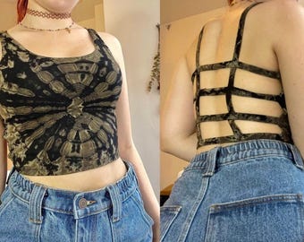 Könnte beinhalten: Ein bauchfreies Top mit Batikmuster in Schwarz und Olivgrün, kombiniert mit einer blauen Jeans. Das Top hat ein einzigartiges Design, und der Rücken hat eine käfigartige Struktur. Die Jeans hat einen Knopfverschluss und Taschen.