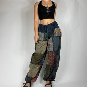May include: Black halter top with a lace-up front and patchwork pants. The pants feature a variety of patterned fabric patches in shades of green, blue, and brown. The pants have a drawstring waist and elastic cuffs at the ankles.