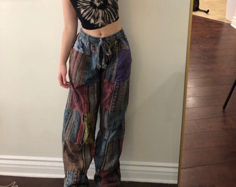 May include: A black and white tie-dye crop top with spaghetti straps paired with patchwork pants. The pants feature a variety of patterned fabric patches in shades of blue, red, and brown. Black sandals complete the outfit.