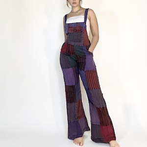 May include: A patchwork denim overall with a wide leg silhouette. The overall is made of different colored denim patches in shades of purple, red, and blue. The overall has a simple white tank top underneath.
