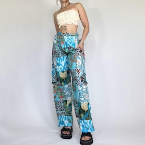 以下が含まれることがあります： 花柄や幾何学模様など、様々な模様が施された青色のパッチワークパンツ。ワイドレッグフィットで、青、赤、緑などの色がミックスされています。クリーム色のストラップレスのトップスと組み合わせています。