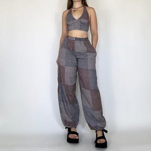 May include: A two-piece outfit featuring a halter top and wide-leg pants. The top is a solid color with a criss-cross design in the front. The pants are a patchwork design with a mix of black, white, and red squares.