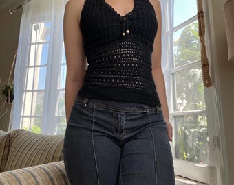 May include: A black halter top with a crochet design. The top has a halter neck and a fitted shape. The top is worn with dark wash denim jeans. The jeans have a high waist and a flared leg.
