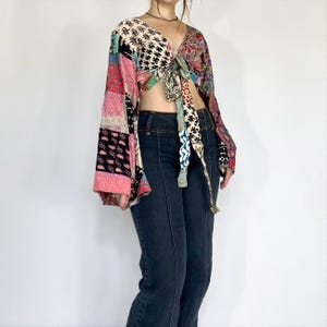 Puede incluir: Top patchwork con lazo frontal y mangas largas acampanadas. El top presenta un cuello en V y una variedad de patrones coloridos, incluyendo diseños florales y geométricos. Las mangas son una mezcla de parches rosas, negros y rojos. El top se ata a la cintura.