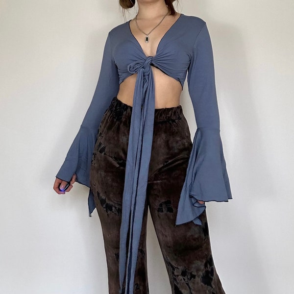 Könnte beinhalten: Ein blaues, langärmliges Crop-Top mit Binde vorne und Glockenärmeln. Das Top ist in der Taille gebunden und wird mit einer braunen Hose getragen.