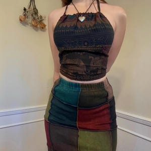 May include: A halter top with a brown, green and blue patterned design. The top has a tie closure at the back of the neck. The model is wearing a multi-coloured patchwork skirt.