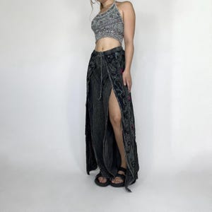 Op de afbeelding: Een haltertop met een paisley patroon in grijstinten en zwart. De top wordt gecombineerd met een lange, splitrok in een donkere grijswas, met geborduurde bloemen- en wervelpatronen. De rok heeft een hoge split.