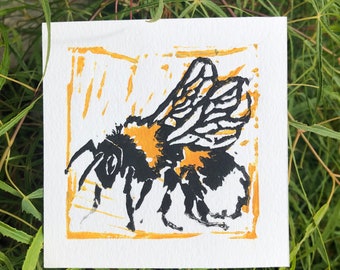 Puede incluir: Un abejorro negro y amarillo con las alas extendidas, impreso en tinta negra y amarilla sobre un fondo blanco con un borde amarillo.