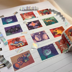 Könnte beinhalten: Eine Sammlung bunter Aufkleber mit verschiedenen Meeresbewohnern, darunter ein Nautilus, eine Qualle, ein Seepferdchen, ein Kugelfisch und eine Fangschrecke. Die Aufkleber sind auf einem Notizbuch mit weißem Hintergrund angeordnet und von schillernden, holografischen Akzenten umgeben.