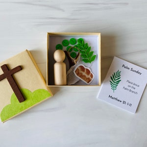 May include: A Palm Sunday themed craft kit. The kit includes a wooden cross, a box with a wooden peg doll, green buttons, felt leaves, and a printed card with the text "Palm Sunday".