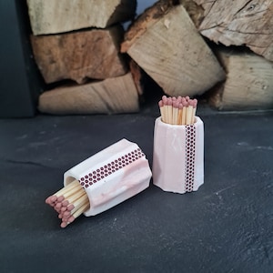 May include: Two pink ceramic matchstick holders with a brown honeycomb pattern. One holder is filled with matches.